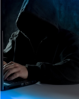a hooded figure at a laptop carrying out a phishing attack