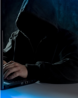 hooded-hacker-phishing a hooded figure at a laptop carrying out a phishing attack